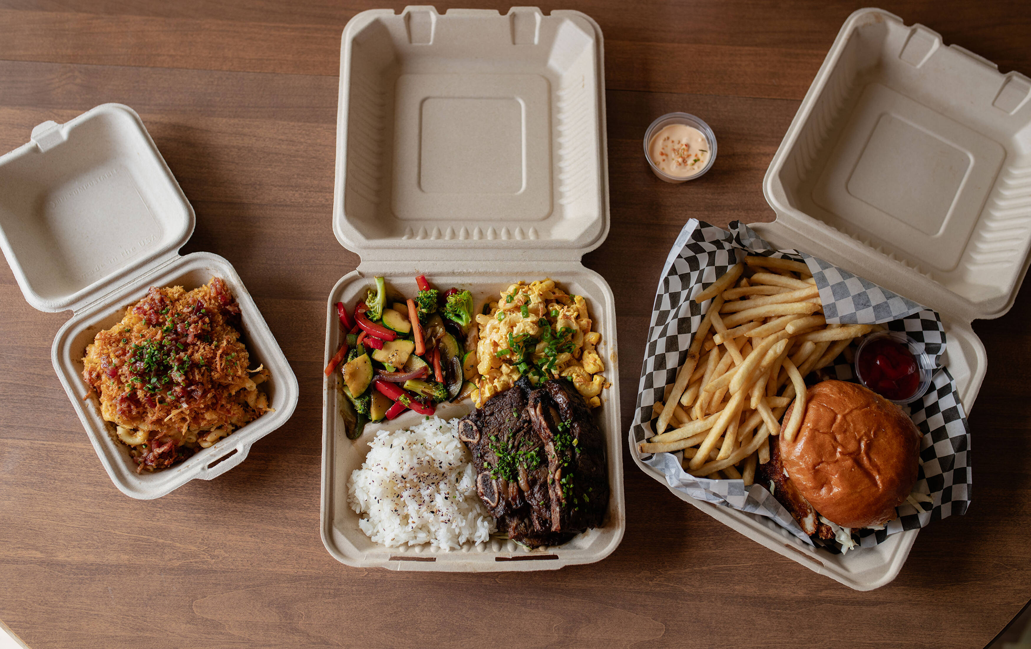 A full Cuisine Collective spread of kalbi ribs, loaded mac, and a katsu burger with fries
